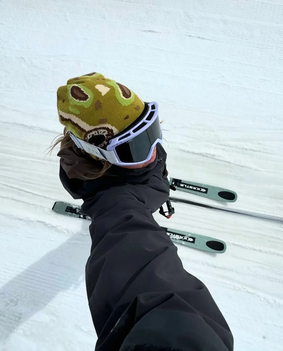 Top-down POV shot of a skier in a green Two Frogs beanie carving fresh snow